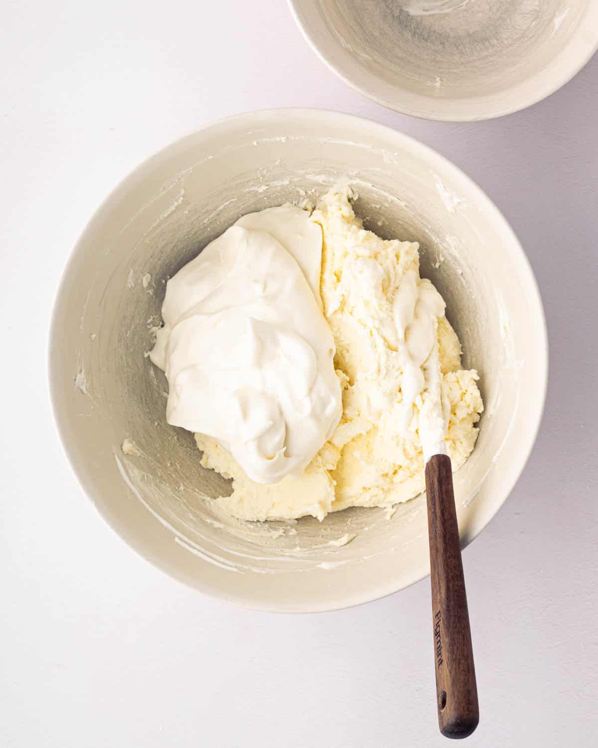 A white bowl with whipped cream and mascarpone and a wooden spatula.