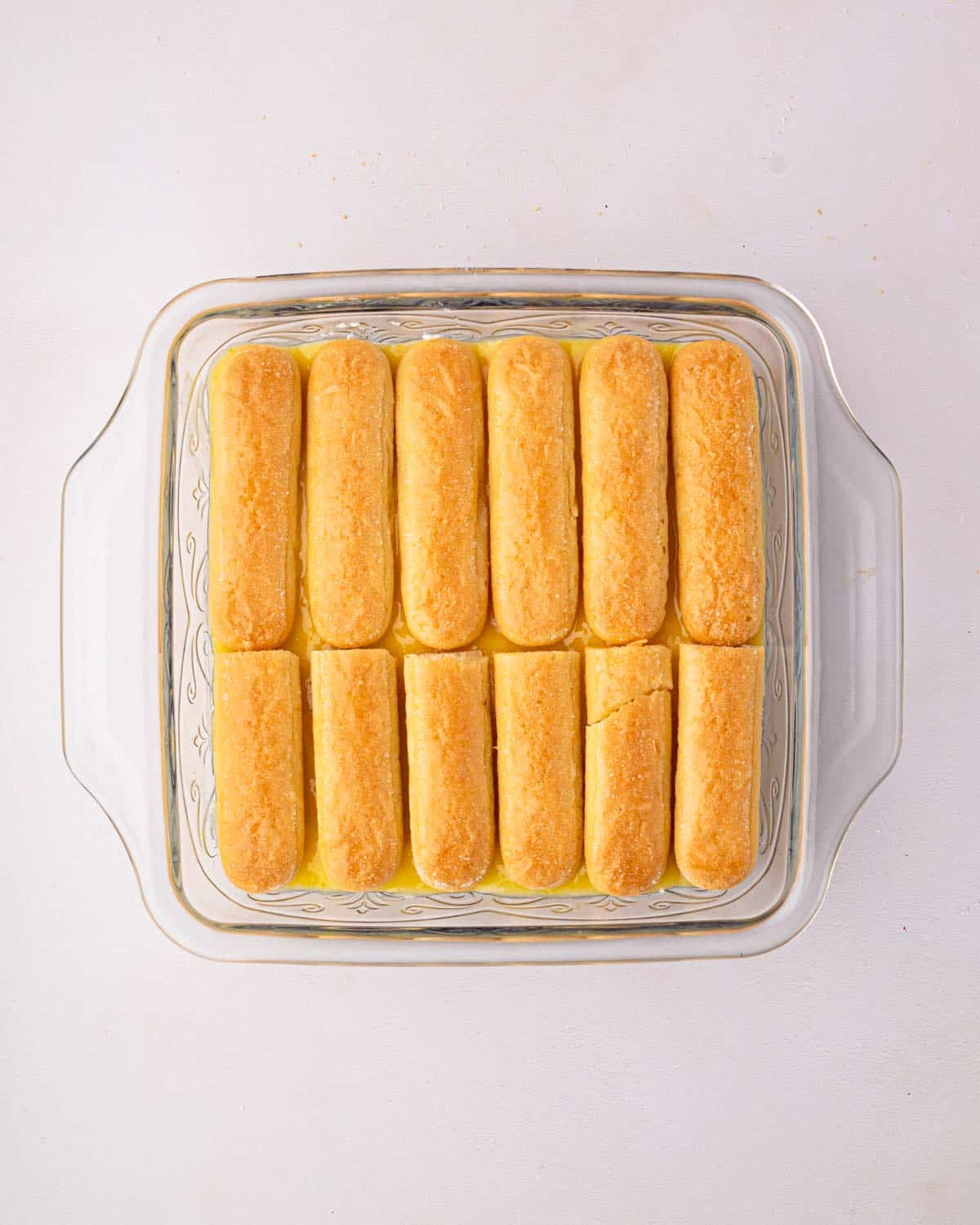 A glass baking dish with layers of lemon curd, mascarpone whipped cream, and dipped ladyfingers for lemon tiramisu.