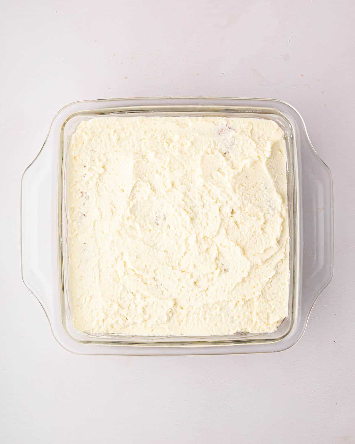 Mascarpone whipped cream is spread on top of a lemon tiramisu in a glass baking dish.