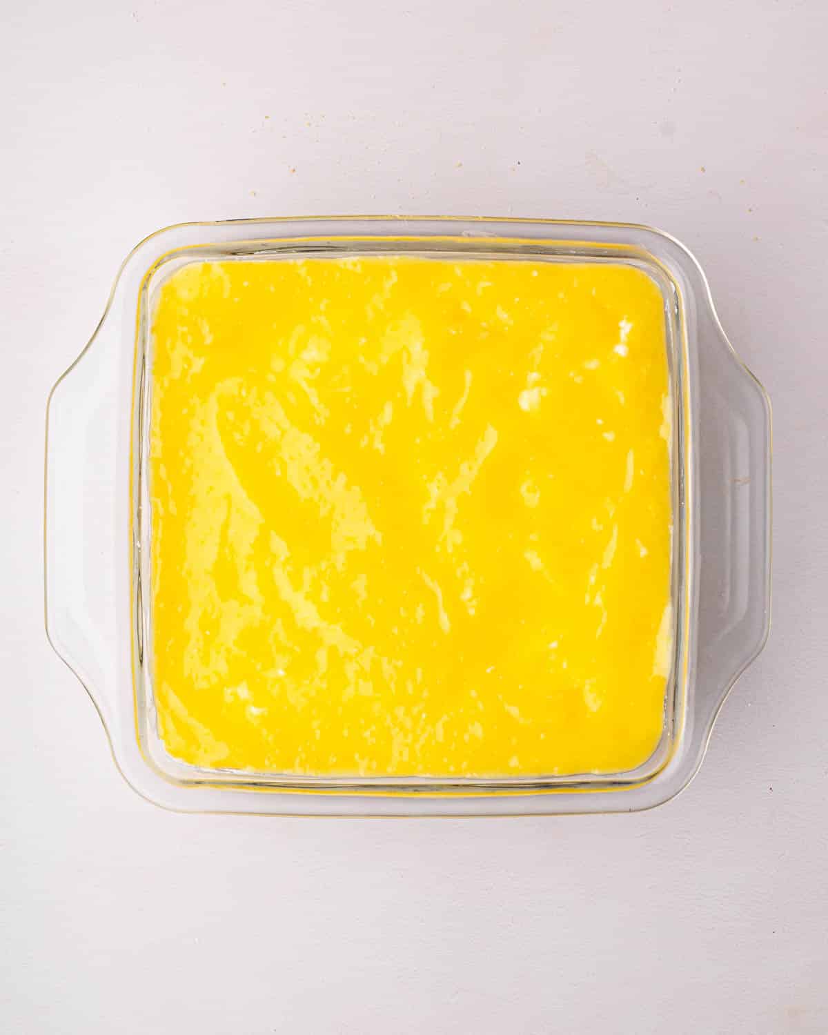 A glass baking dish with lemon curd spread on top for lemon tiramisu.