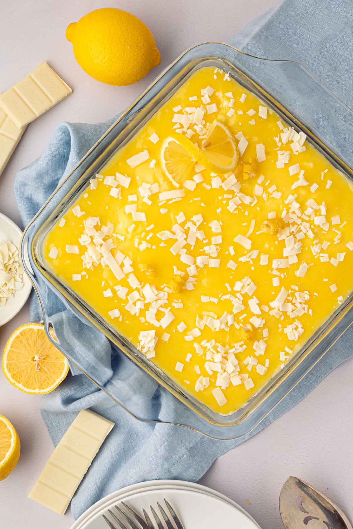 Finished lemon tiramisu with white chocolate shavings on top, a blue linen underneath, and fresh lemons.