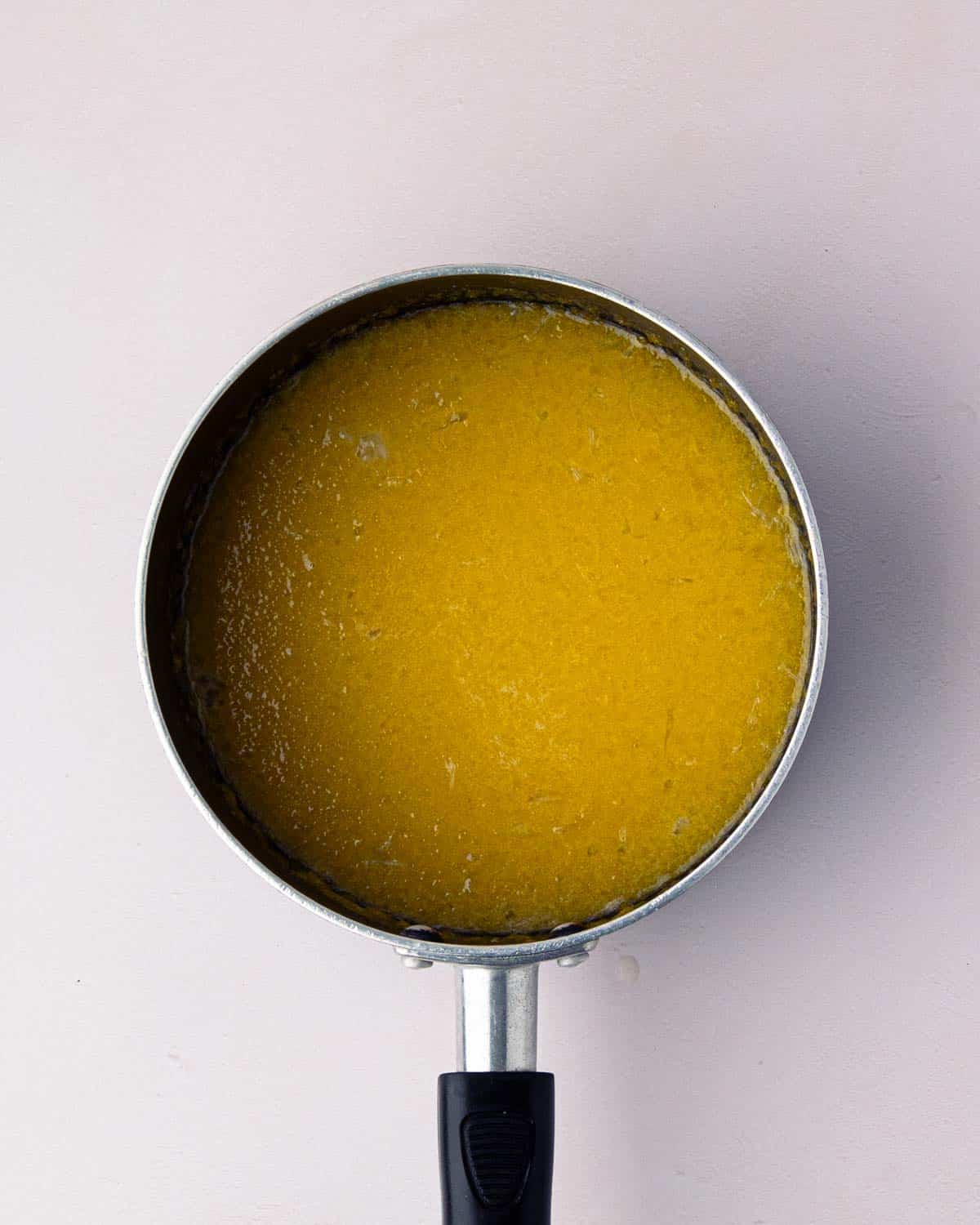 Simmering lemon curd in a black saucepan.