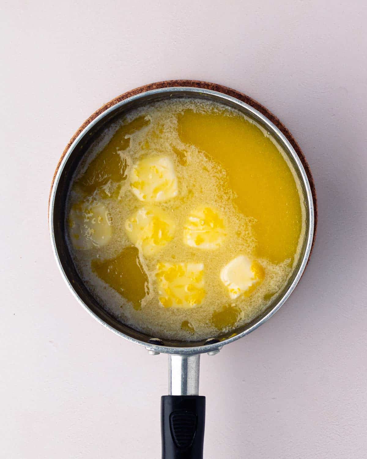 A black saucepan with lemon curd ingredients cooking and butter added.