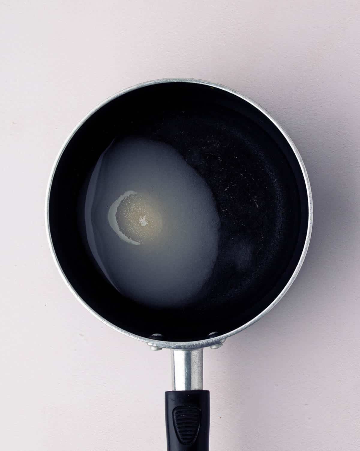A small black skillet with water and sugar melting.