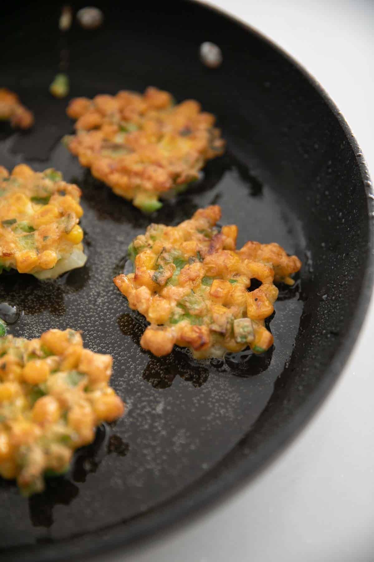 Flipped corn fritters cooking in a large skillet.