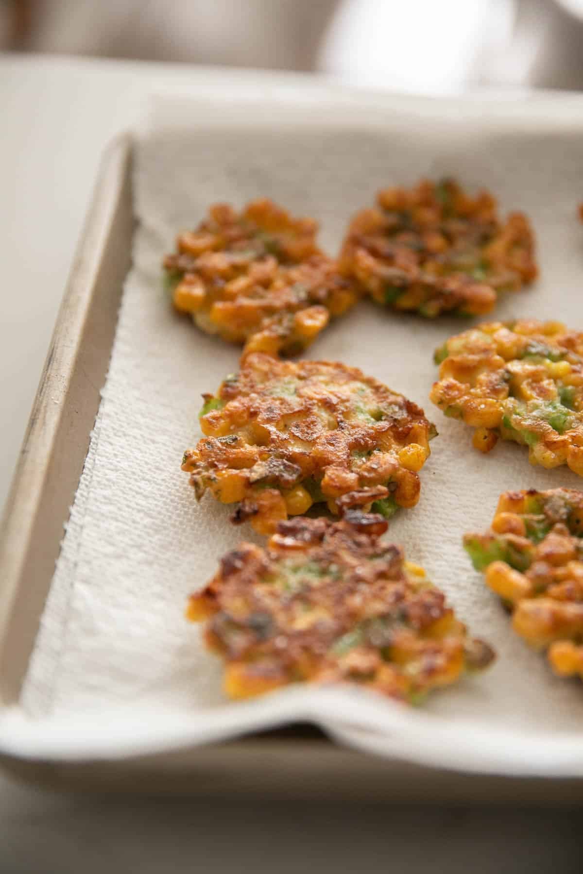 A paper towel-lined baking sheet with corn fritters.