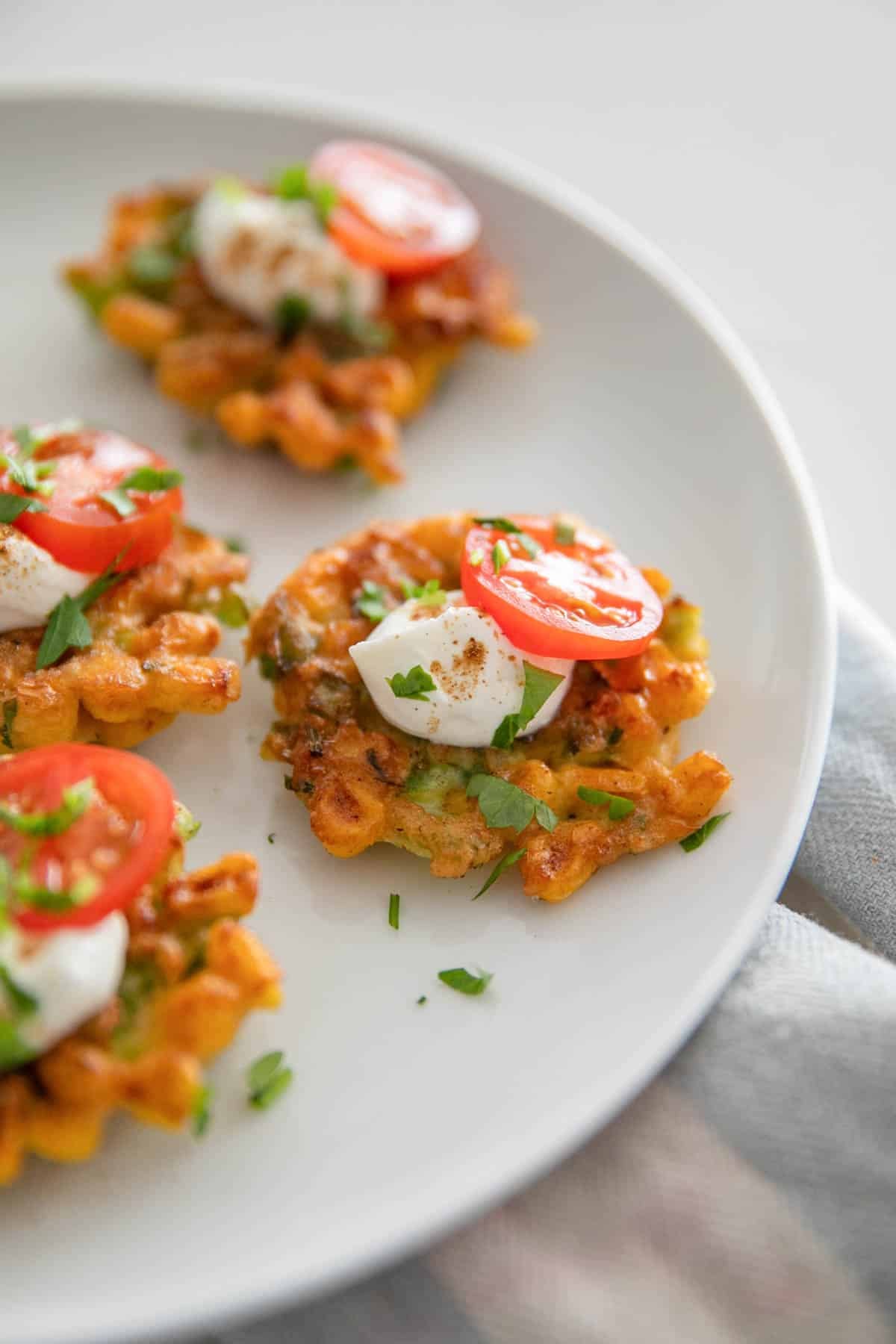 Close up image of corn fritters with cherry tomato and sour cream on top.
