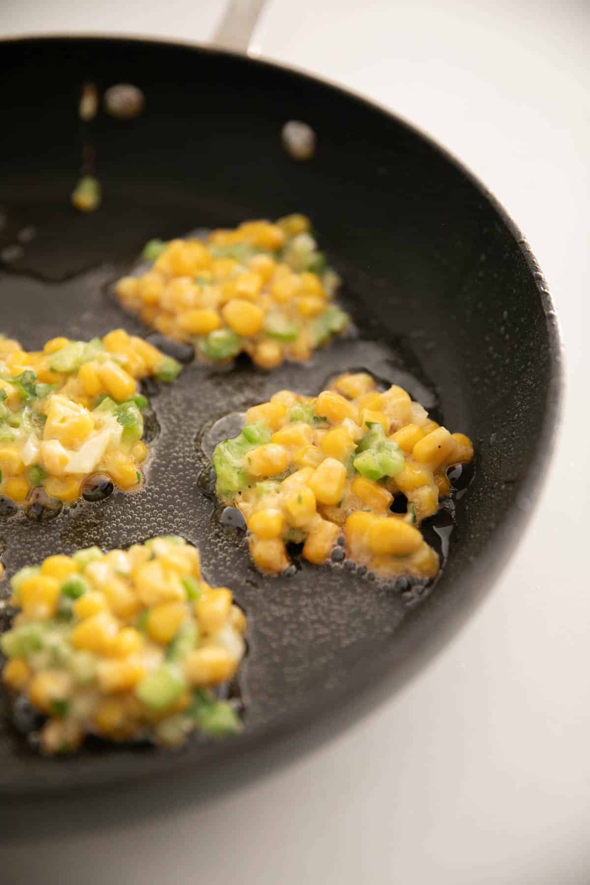 A large skillet with corn fritters cooking.
