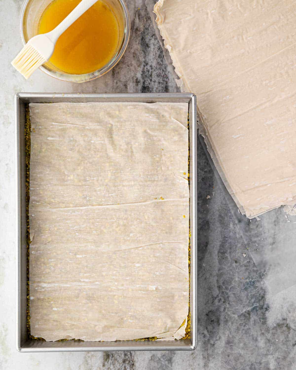 A baking dish with a sheet of phyllo layered over pistachios.