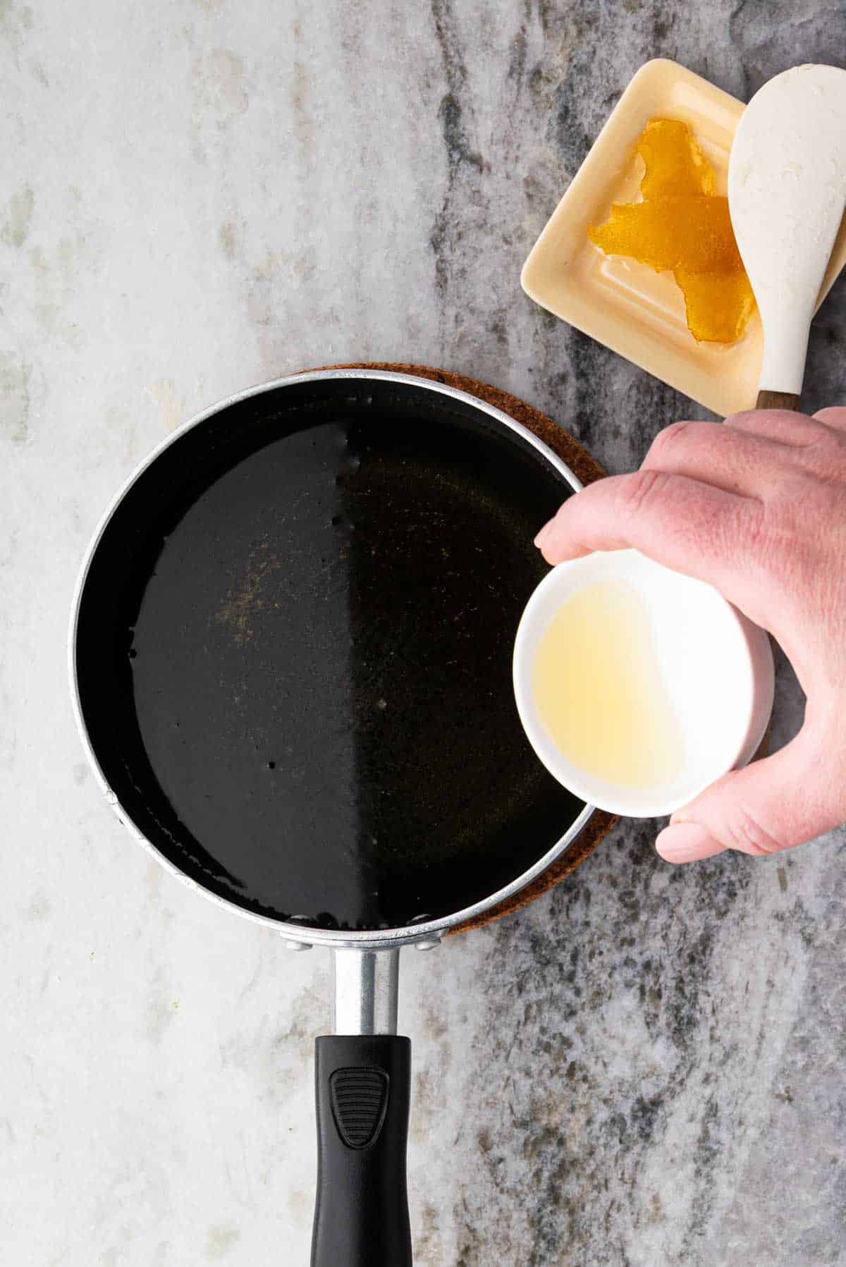 A saucepan with simple syrup and a hand adding lemon juice.