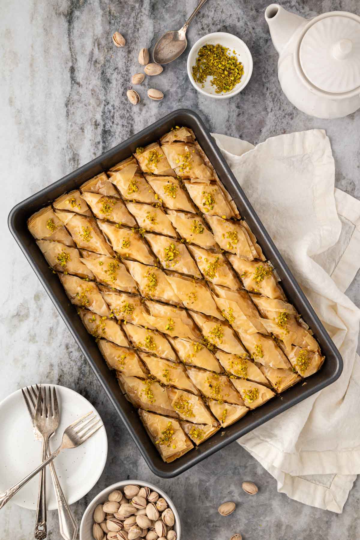 A pan with pistachio baklava with plates and forks around it.