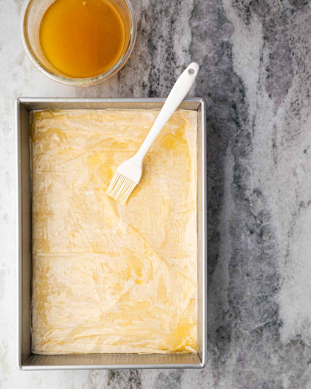 A brush with layers of phyllo and pistachio filling. The brush is resting in the pan.