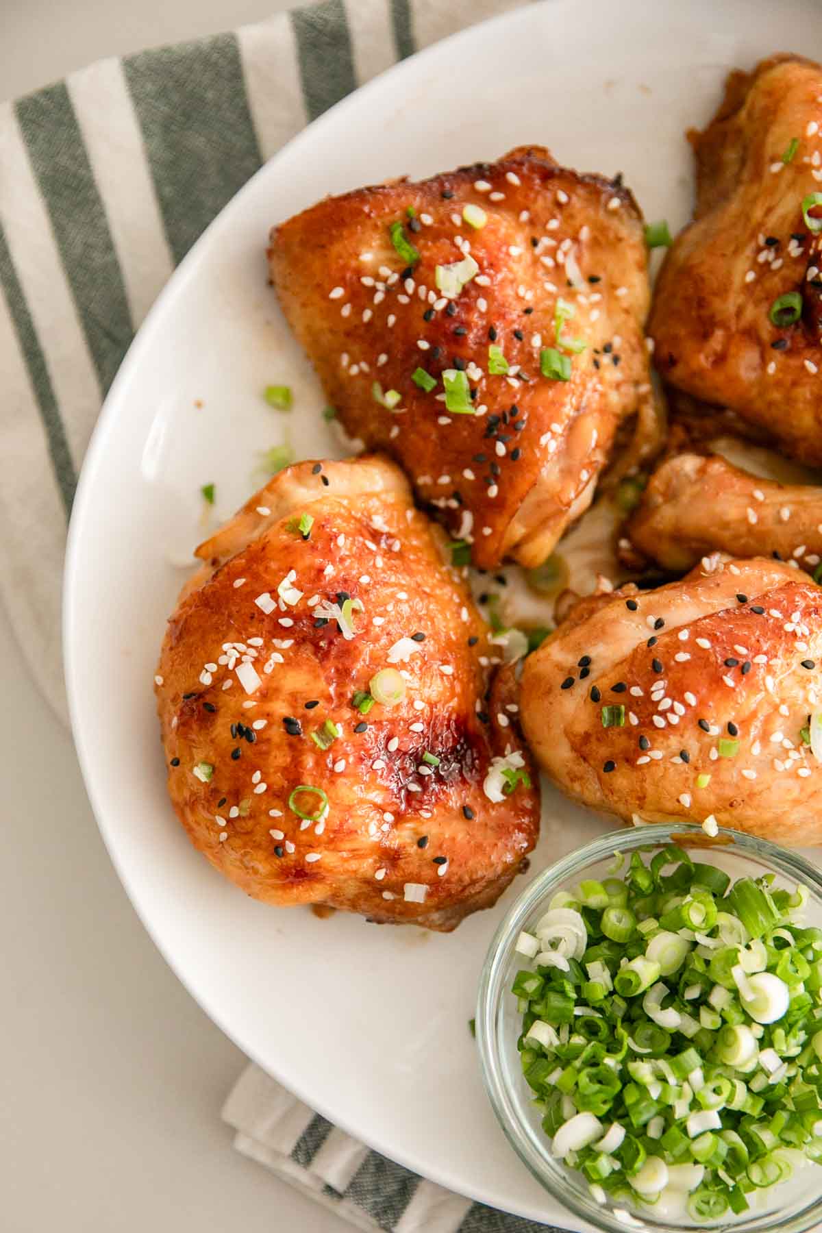 A white plate of roasted miso chicken with a bowl of scallions on the side.