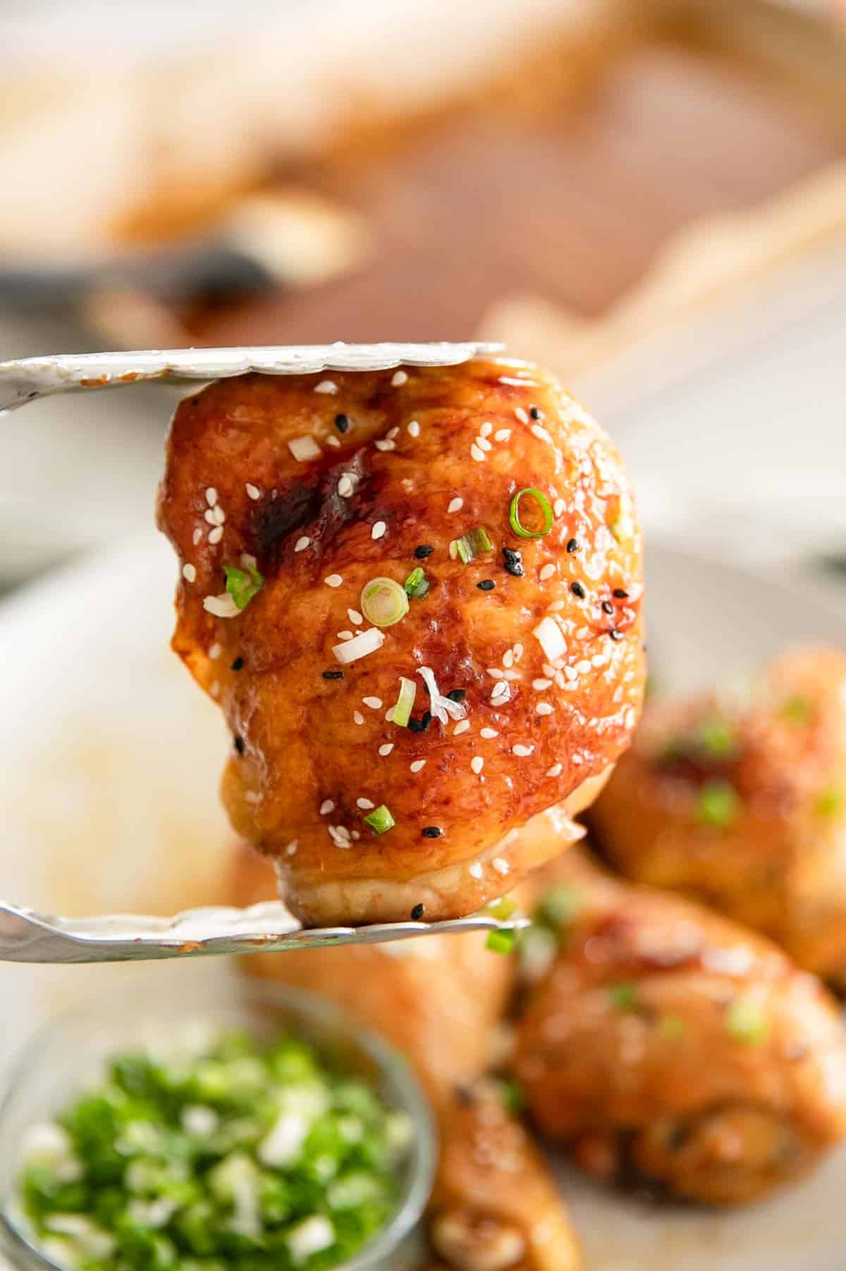 Tongs holding up a miso chicken thigh.