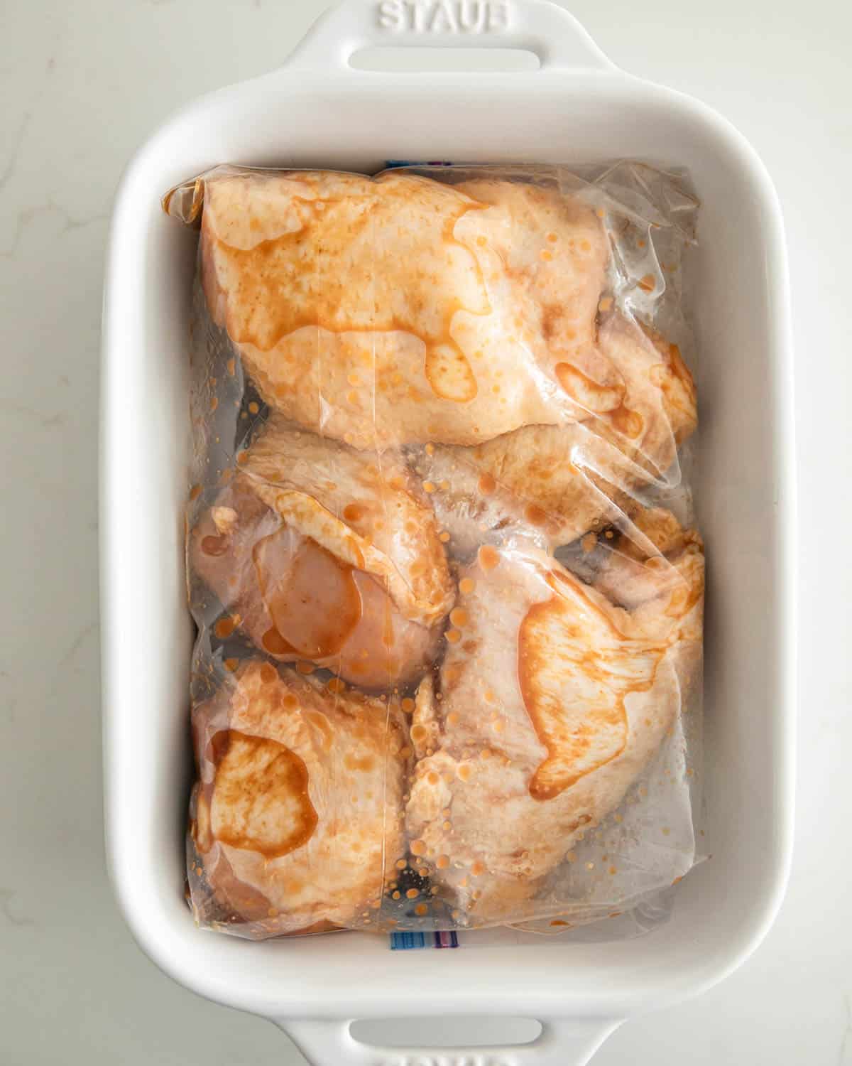 A bag of miso marinated chicken thighs in a white baking dish.