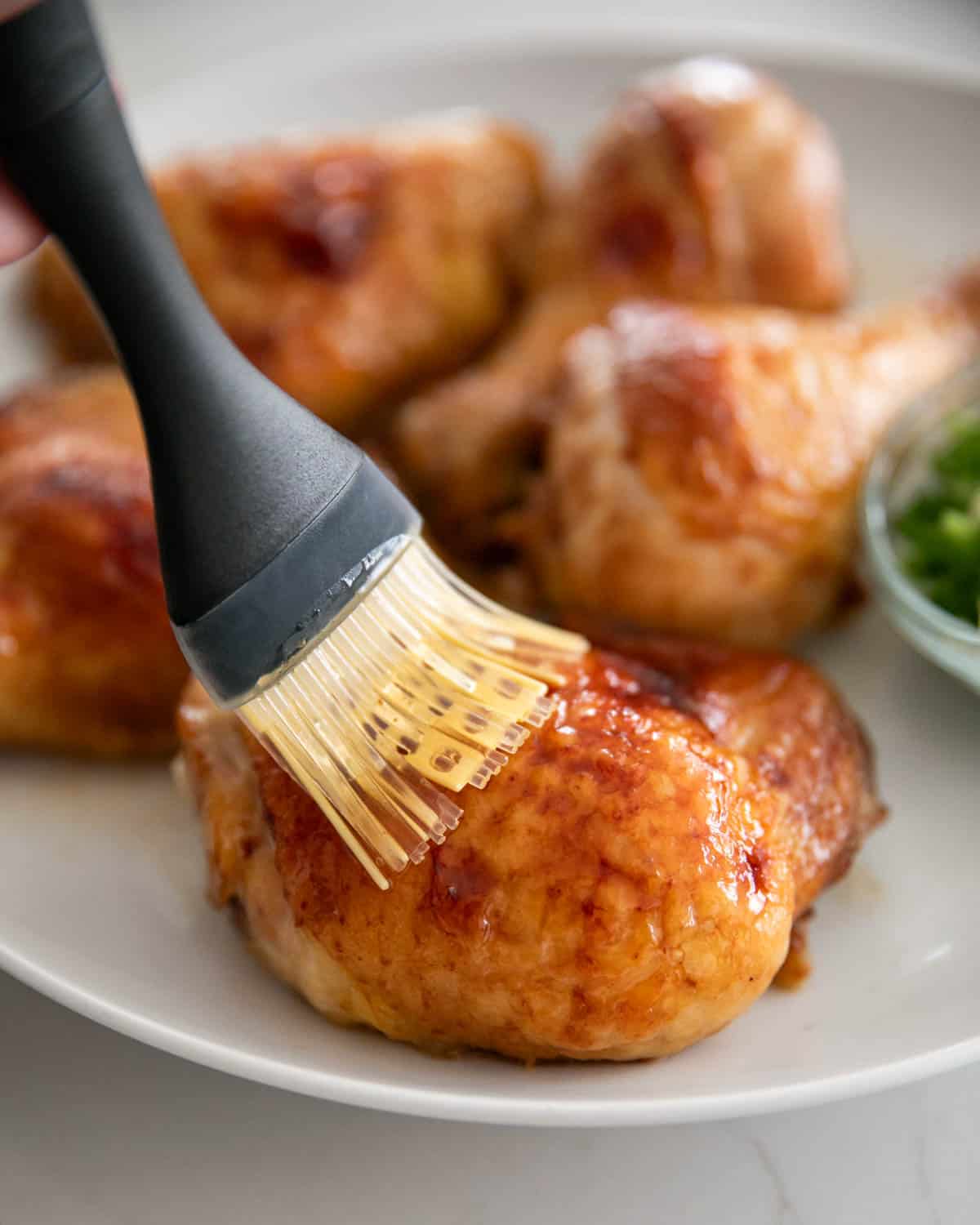 A brush adding miso glaze to the chicken thighs on a white plate.