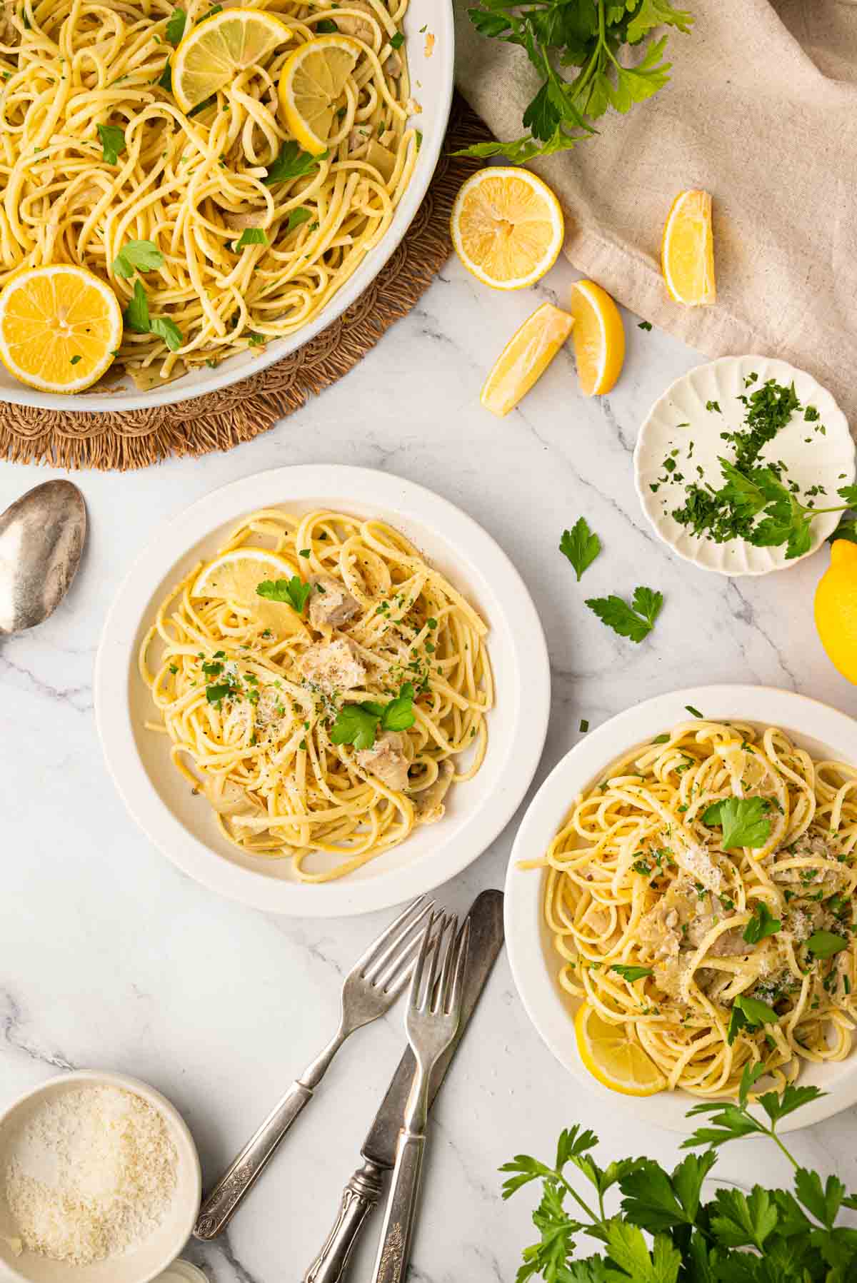 Overhead image of lemon artichoke pasta in two white bowls with a bigger serving bowl of pasta in the back.