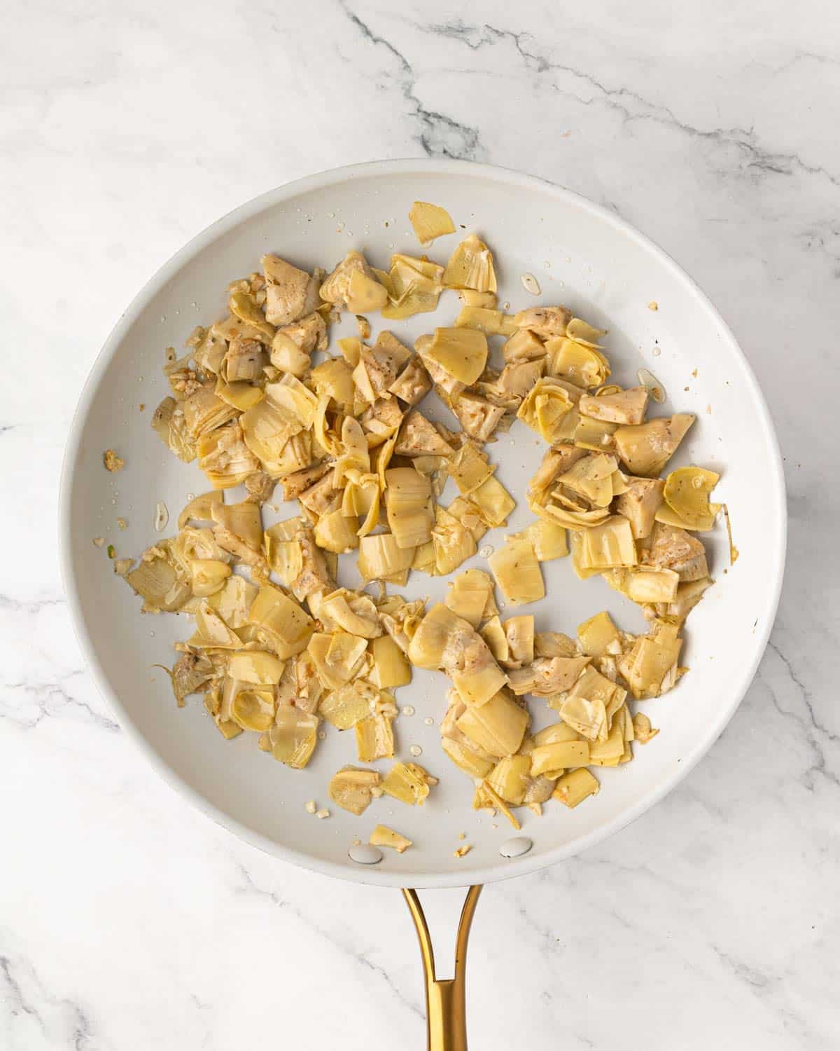 Cooked garlic and artichoke hearts in a white skillet.