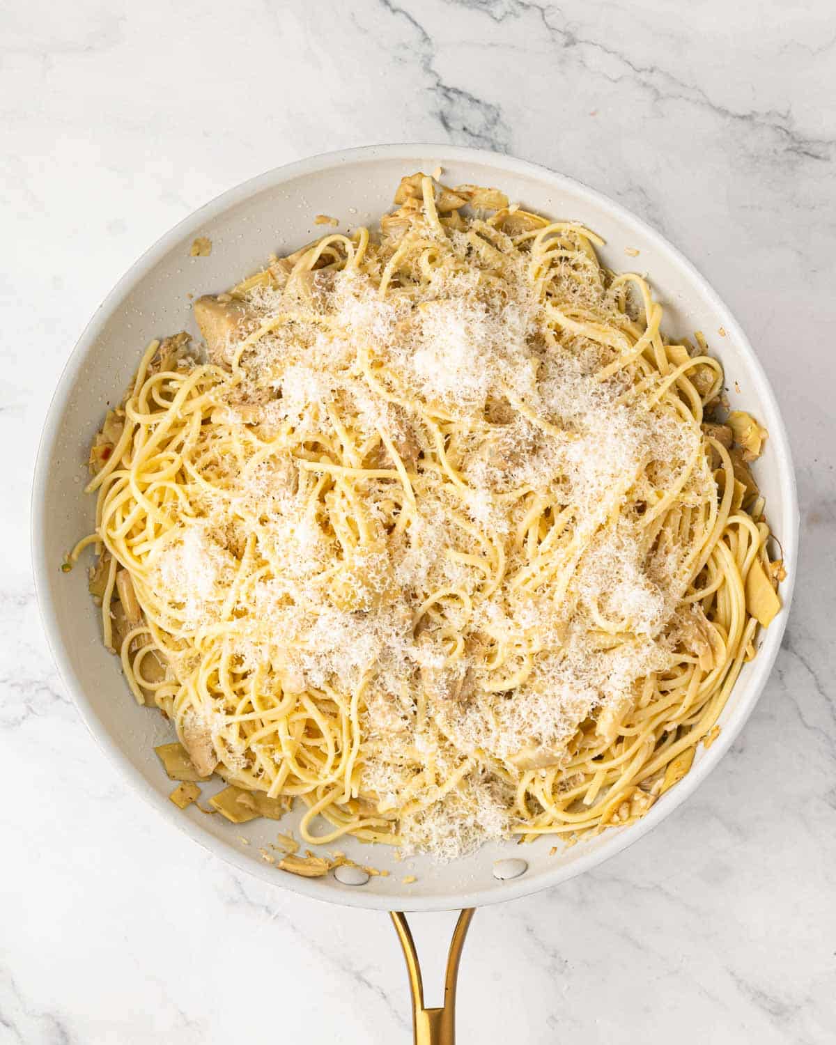 A white skillet with pasta and artichokes and grated parmesan cheese on top.