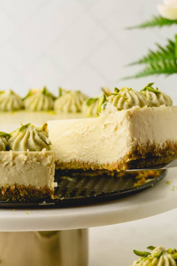A slice of pistachio cheesecake being taken out with a cake server.