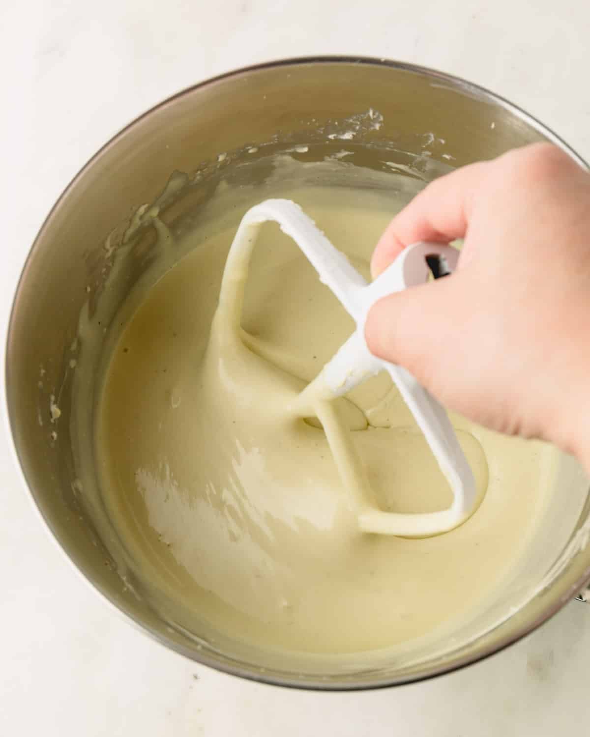 A hand is adding the paddle attachment to the stand mixer with the pistachio cheesecake filling.