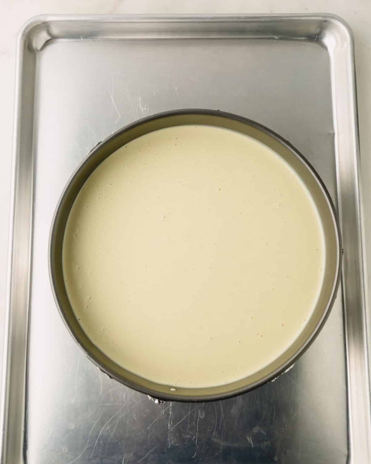 A baking sheet with a springform pan with pistachio cheesecake.