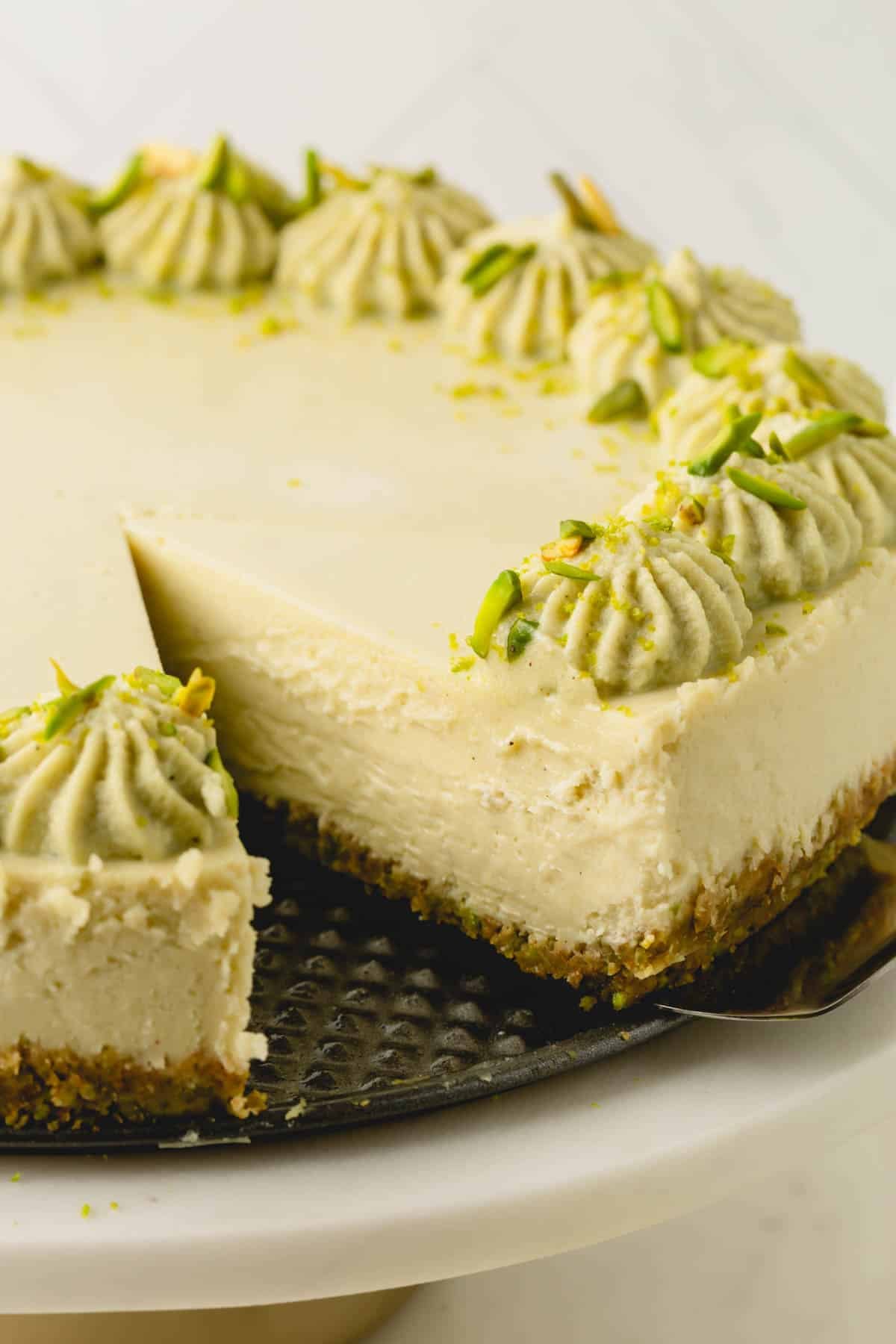 Close up image of a slice of pistachio cheesecake being removed with a cake server.