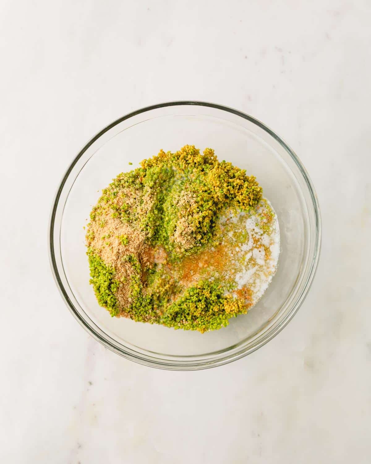 A glass bowl with ingredient for pistachio graham cracker crust.