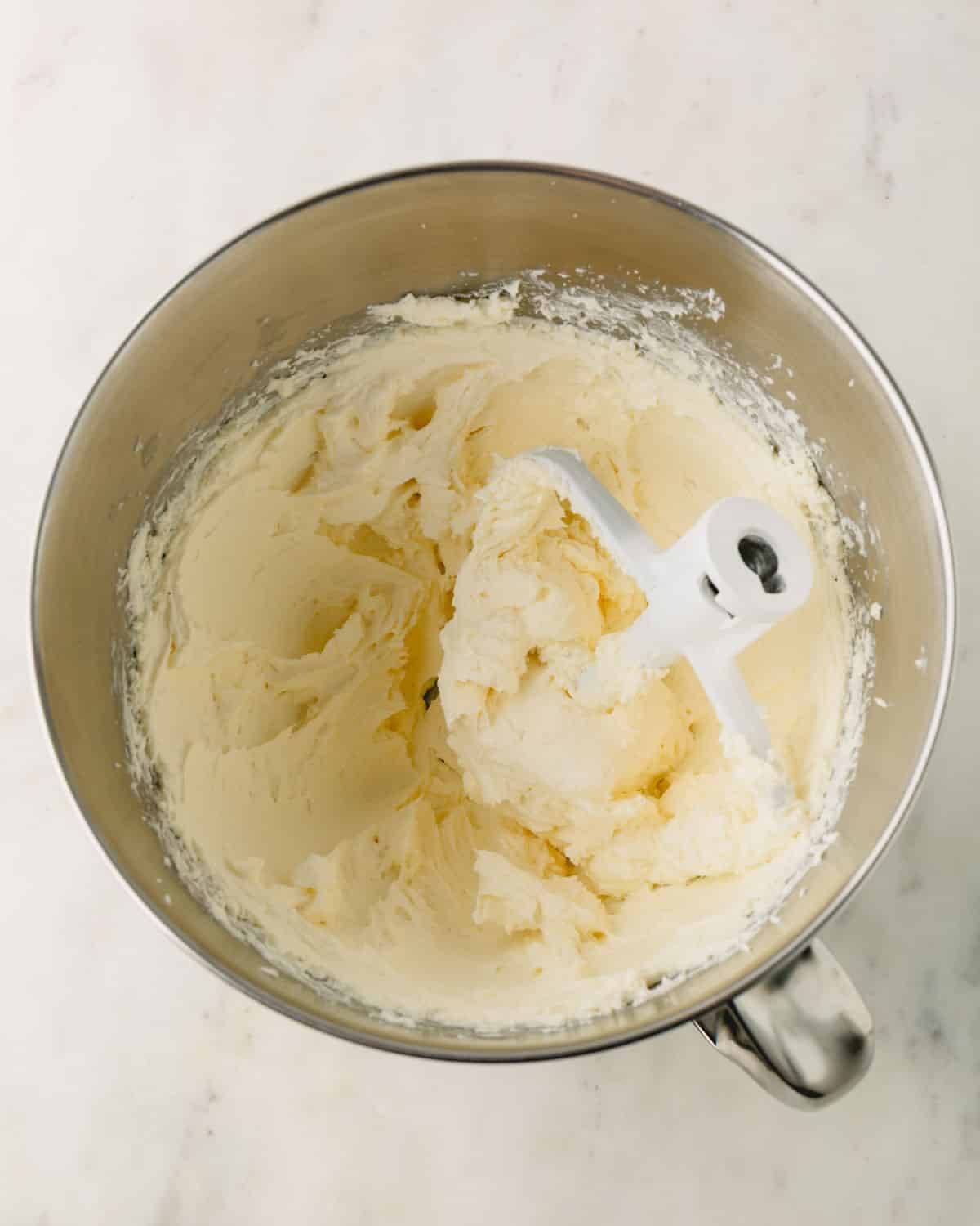 A stand mixer with cream cheese filling for cheesecake and a paddle attachment resting in the bowl.