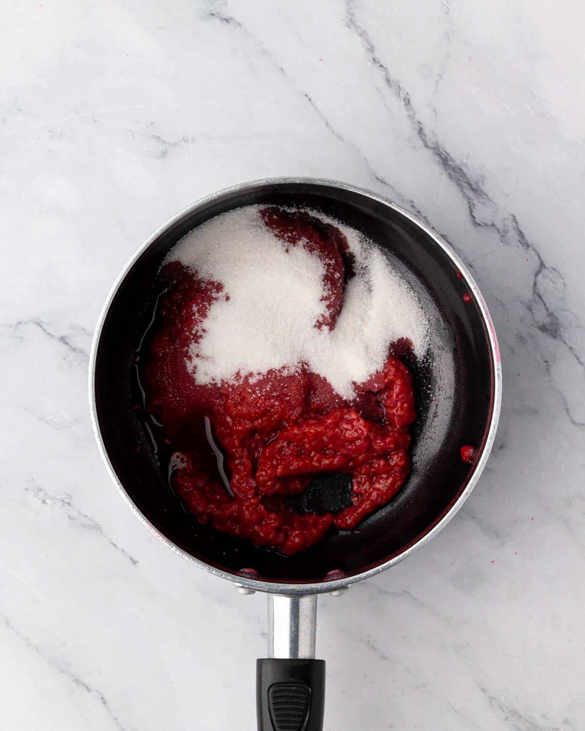 Raspberry pulp with sugar in a saucepan to make raspberry compote.