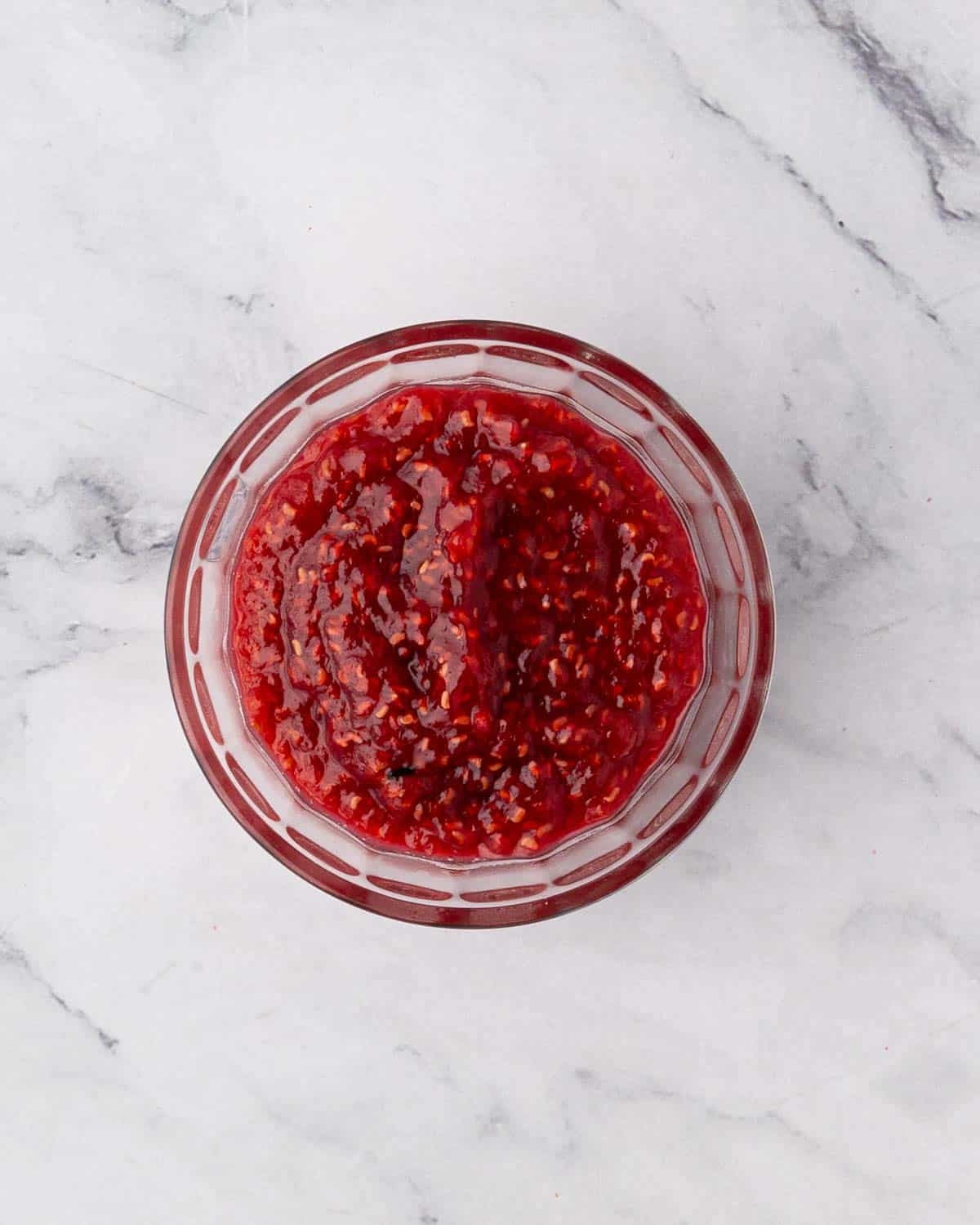 Cooled raspberry compote in a glass bowl.