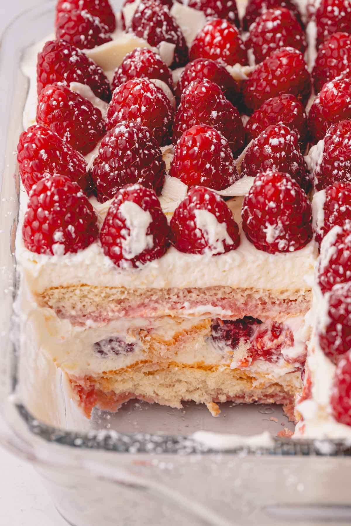 Close up image of a slice taken out of raspberry tiramisu in a glass baking dish.