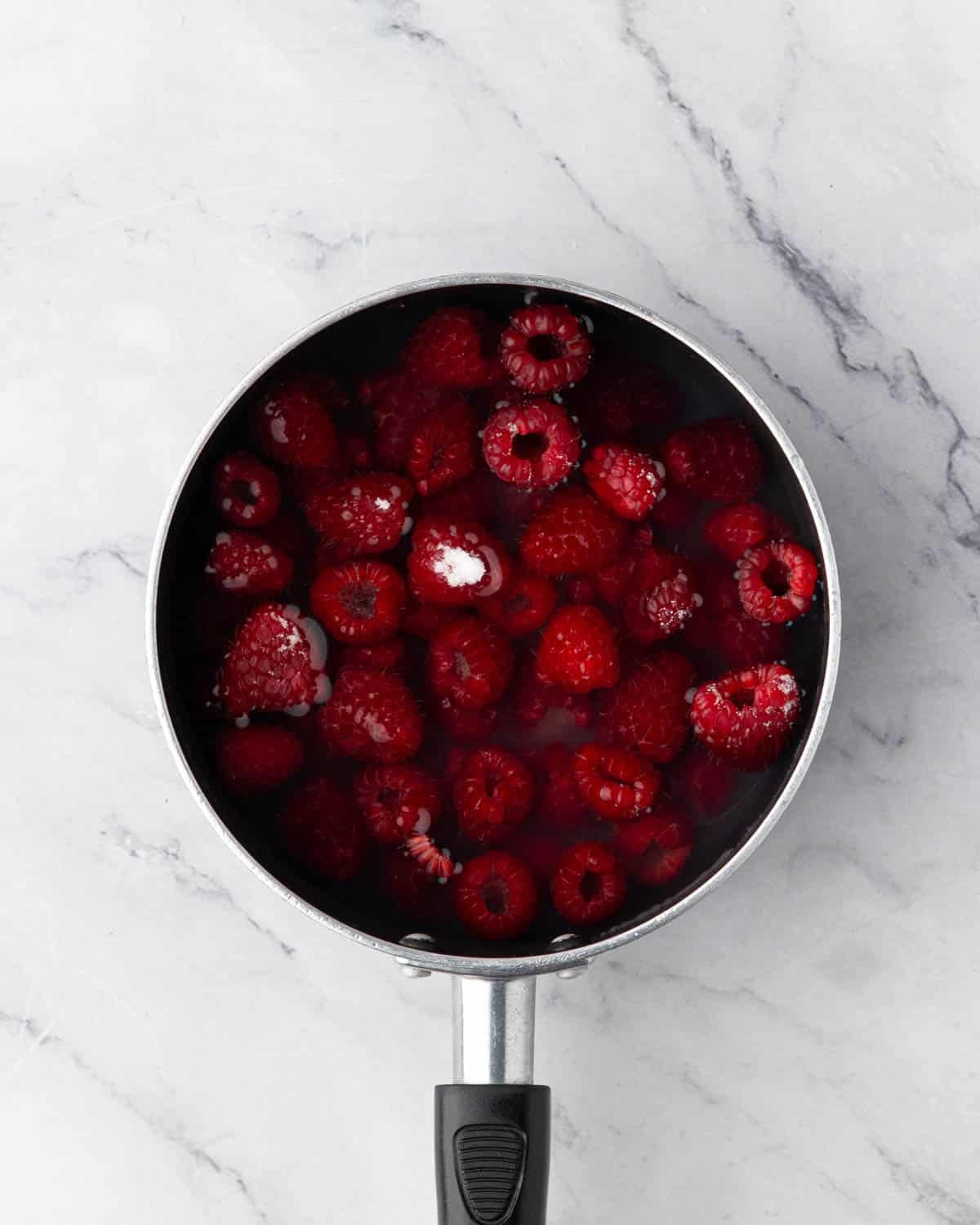 Ingredients for raspberry simple syrup in a black saucepan.