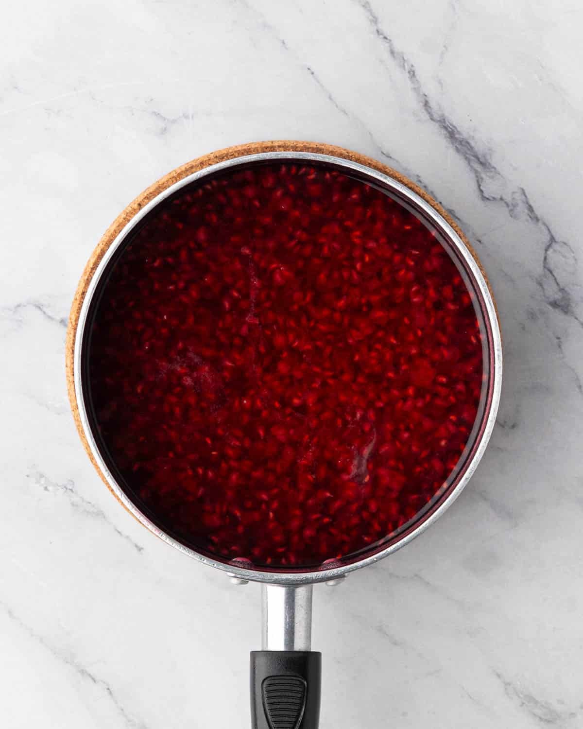 Raspberry simple syrup cooking in a black saucepan.