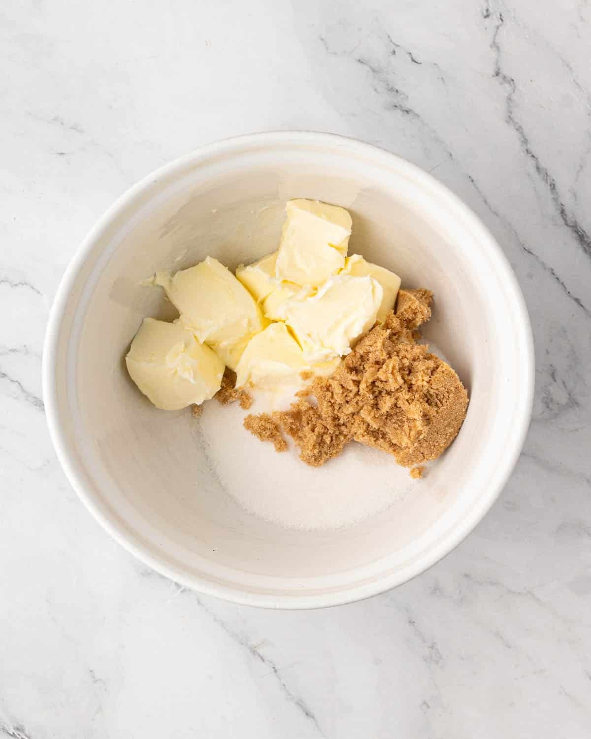 A white bowl with butter, brown sugar, and regular sugar.