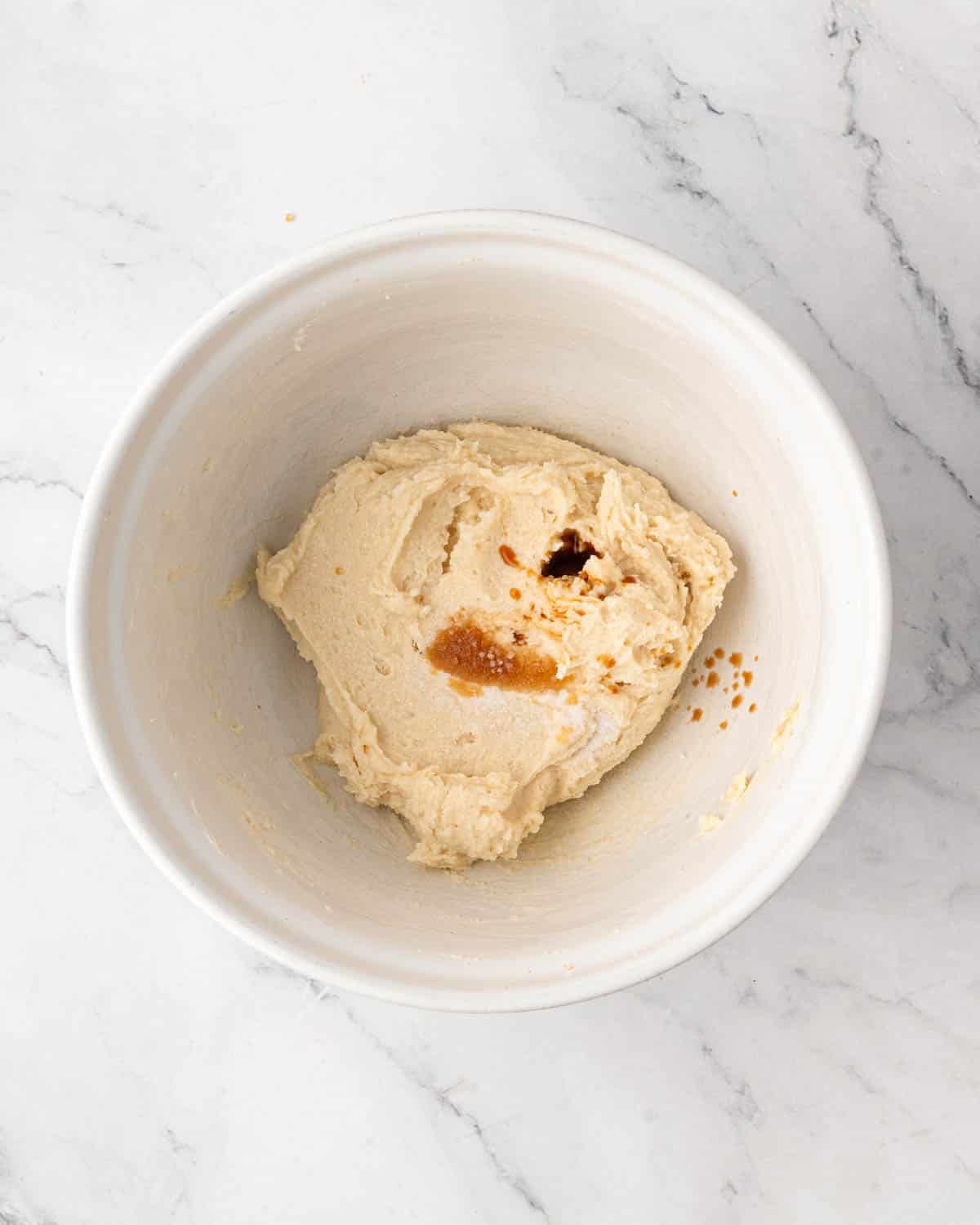 A white bowl with creamed butter and sugar. Vanilla extract and salt is on top.