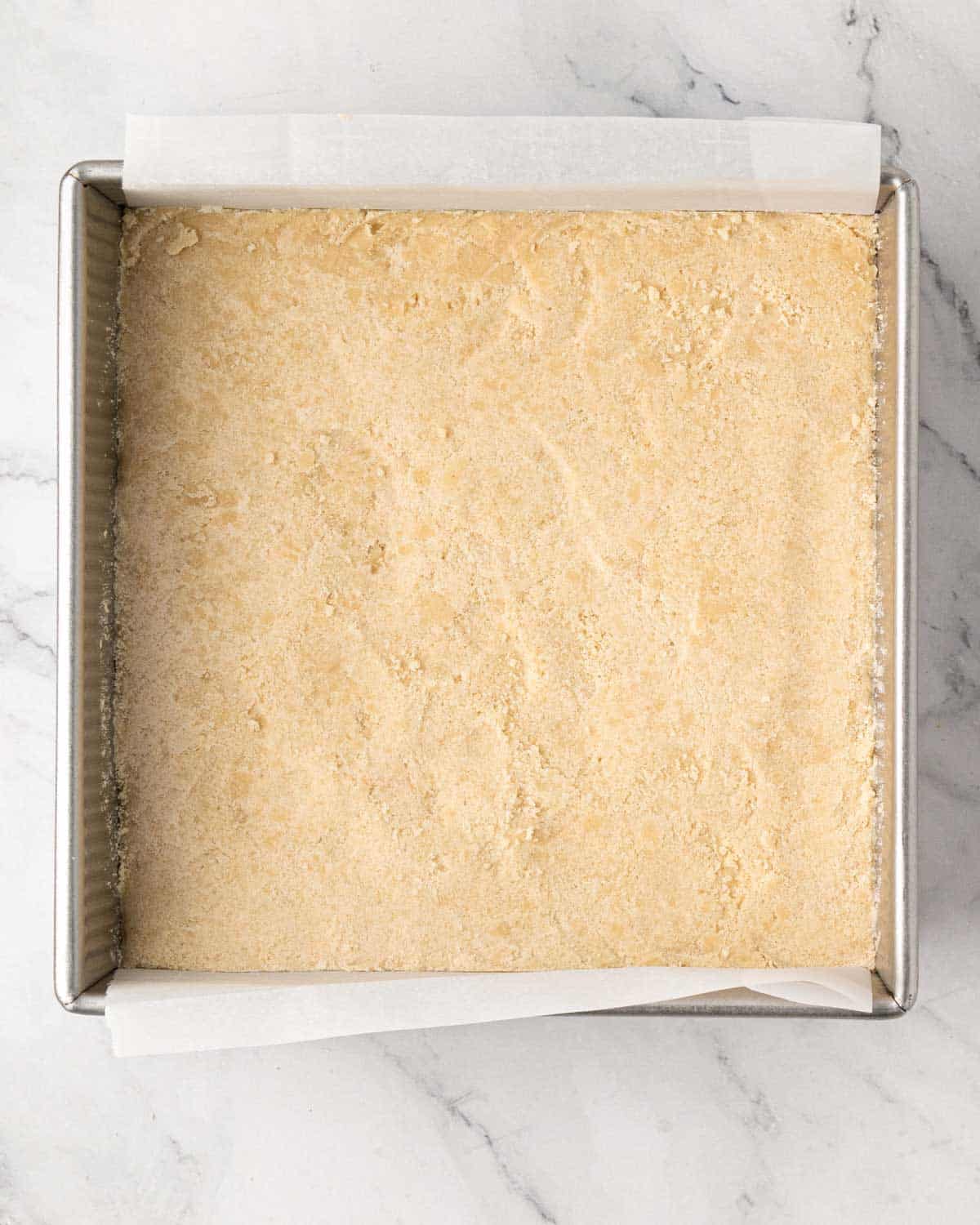 Shortbread cookie mixture pressed into the bottom of a baking dish lined with parchment.