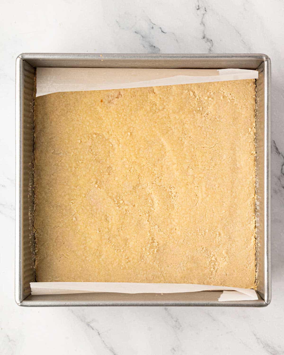 A baking pan with shortbread cookie pressed in the bottom and lined with parchment.