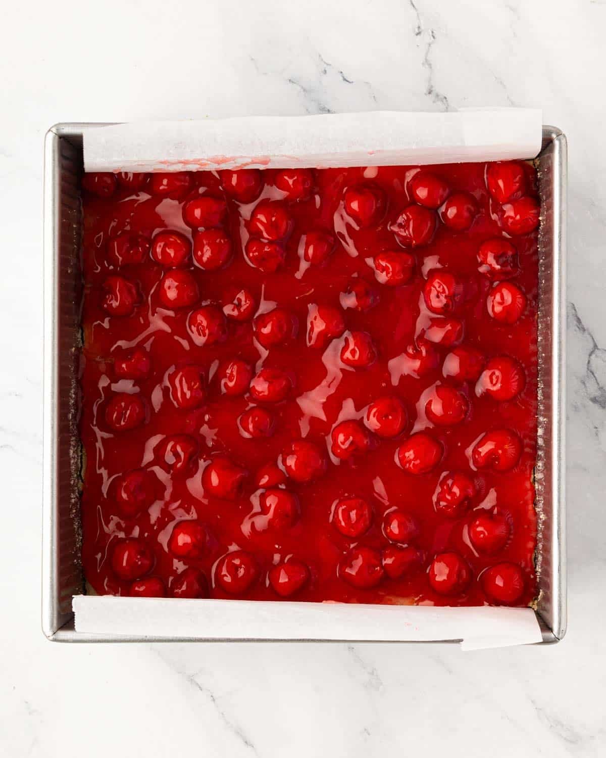 A baking pan with cherry pie bars with cookie crust and cherry pie topping.
