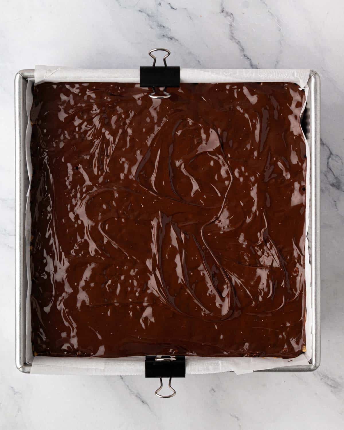 A baking pan with scotcharoos and melted chocolate spread on top.