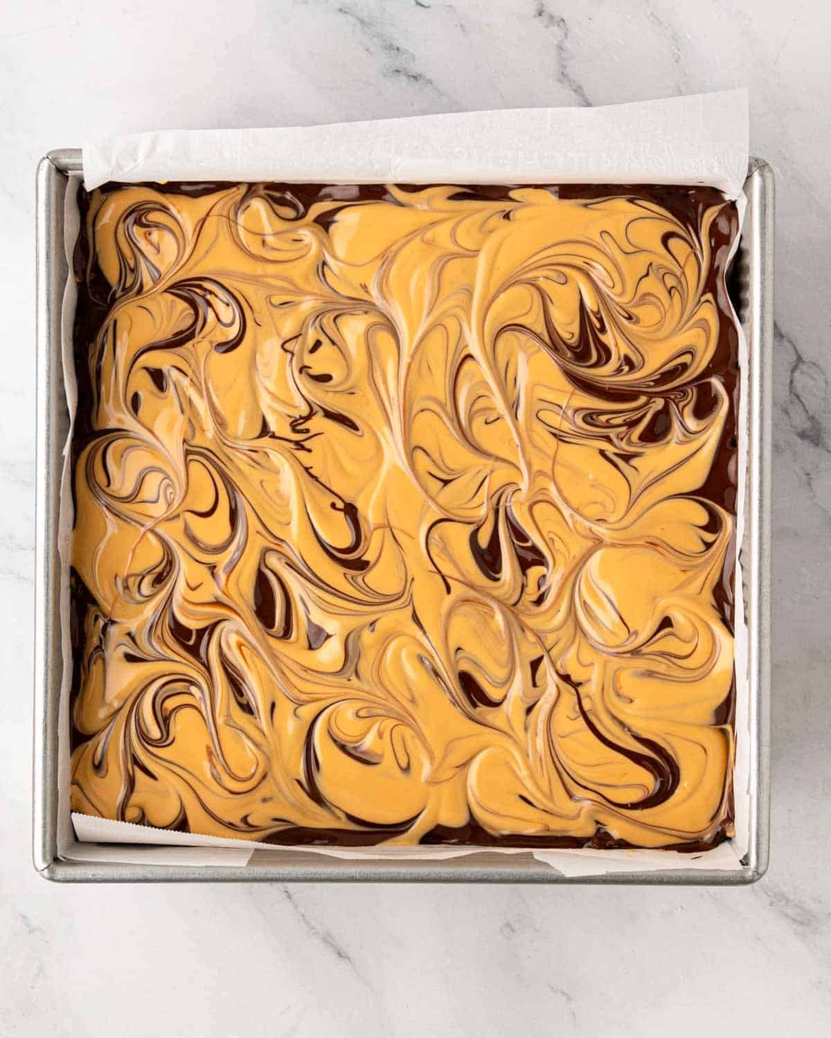 A baking dish lined with parchment paper with scotcharoos ready to set.