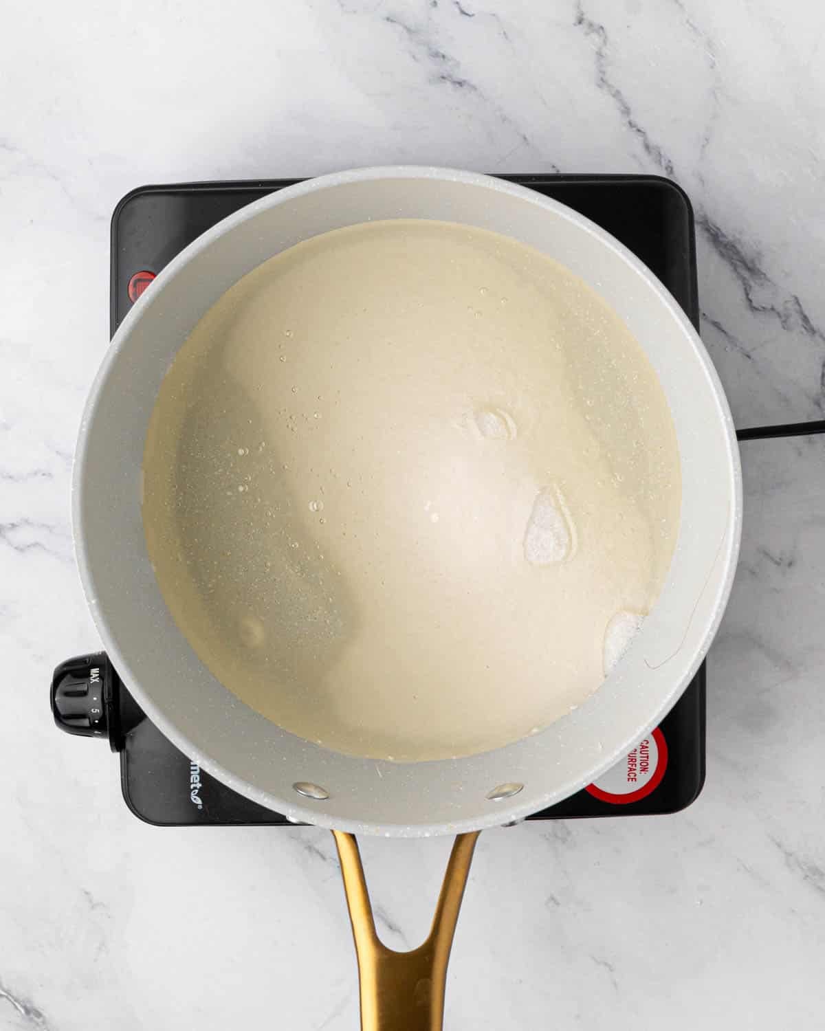 Corn syrup and sugar in a white saucepan on a burner.
