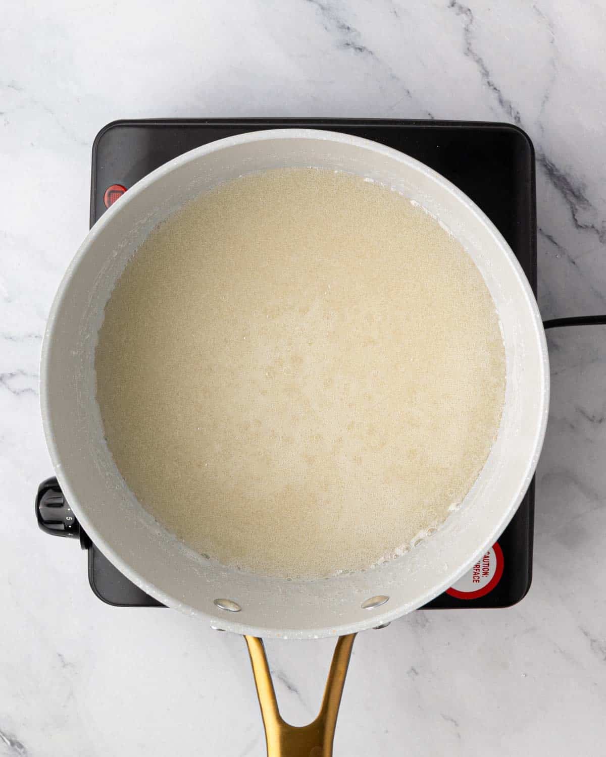 A white saucepan with corn syrup and sugar simmering on an induction burner.