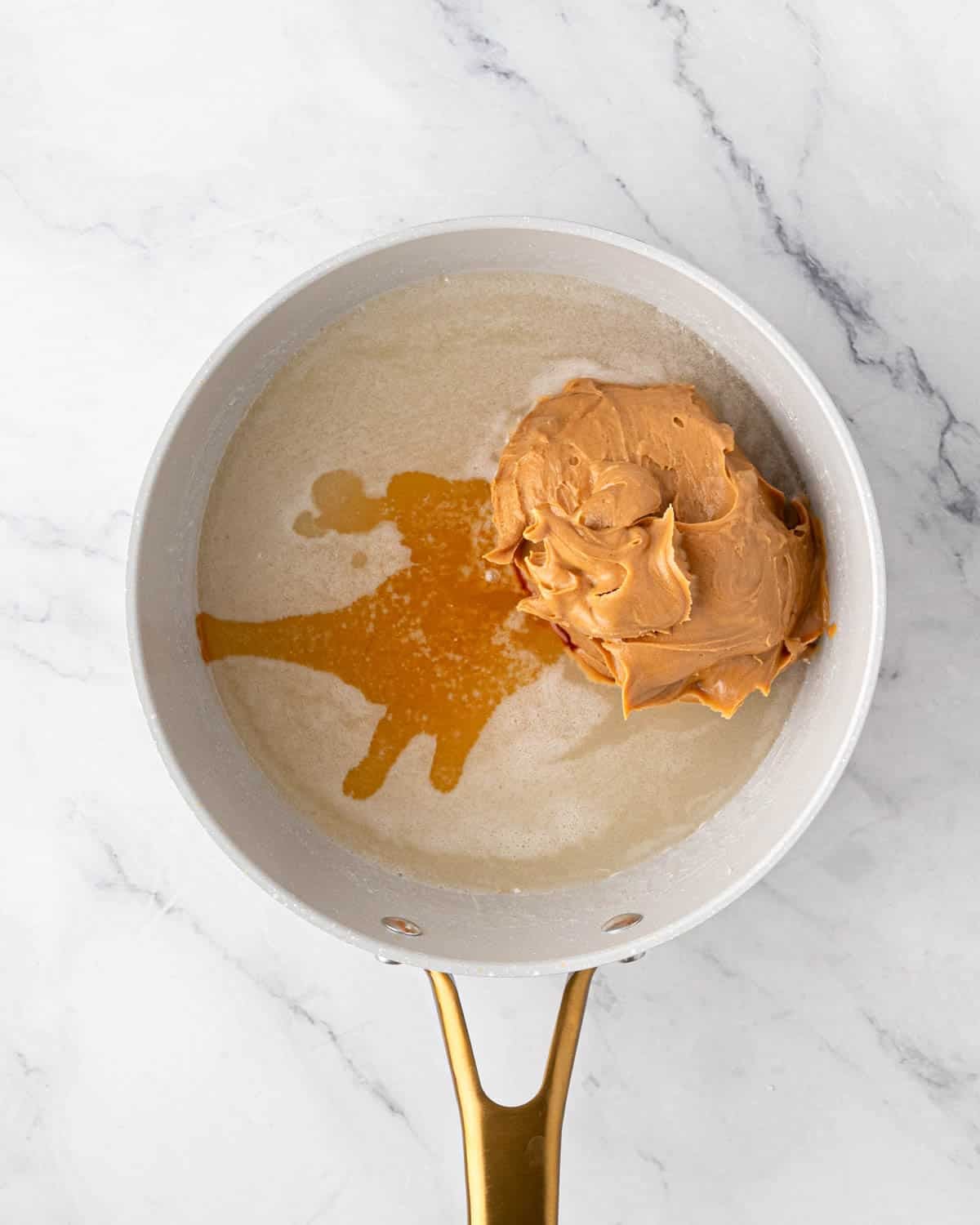 A white saucepan of peanut butter, sugar, corn syrup, and vanilla for scotcharoo base.