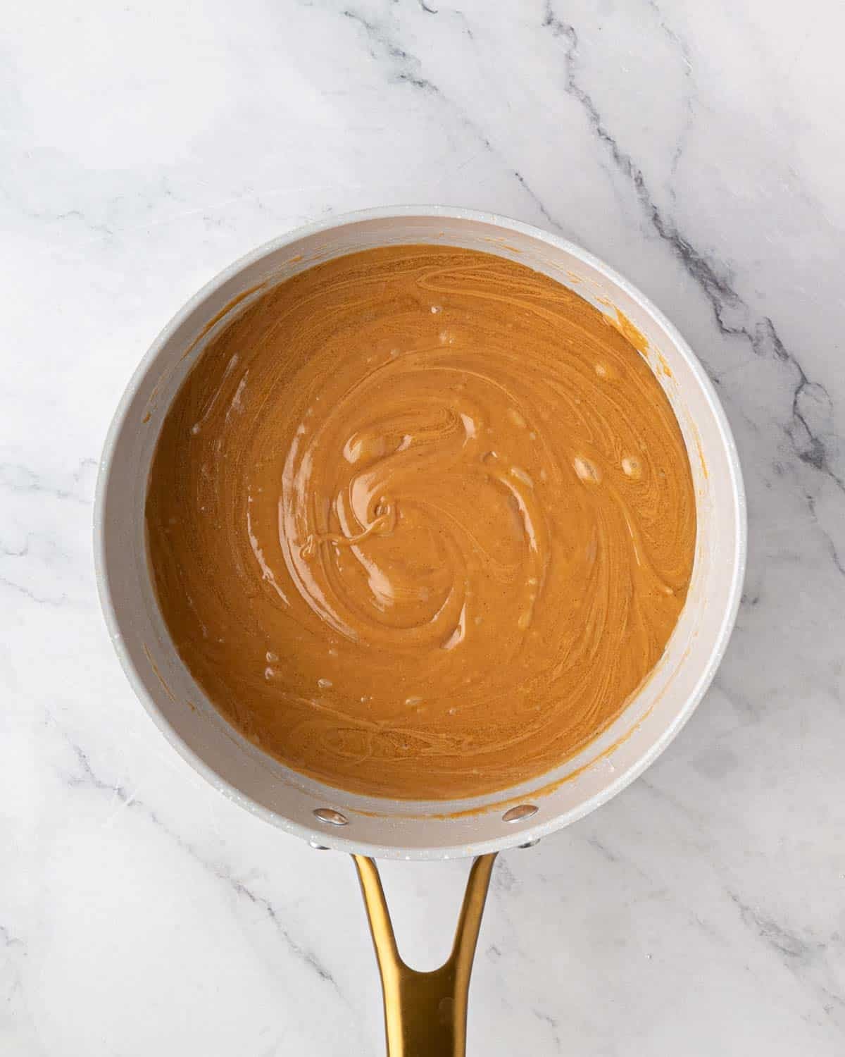 A white saucepan of melted peanut butter mixture for scotcharoos. 