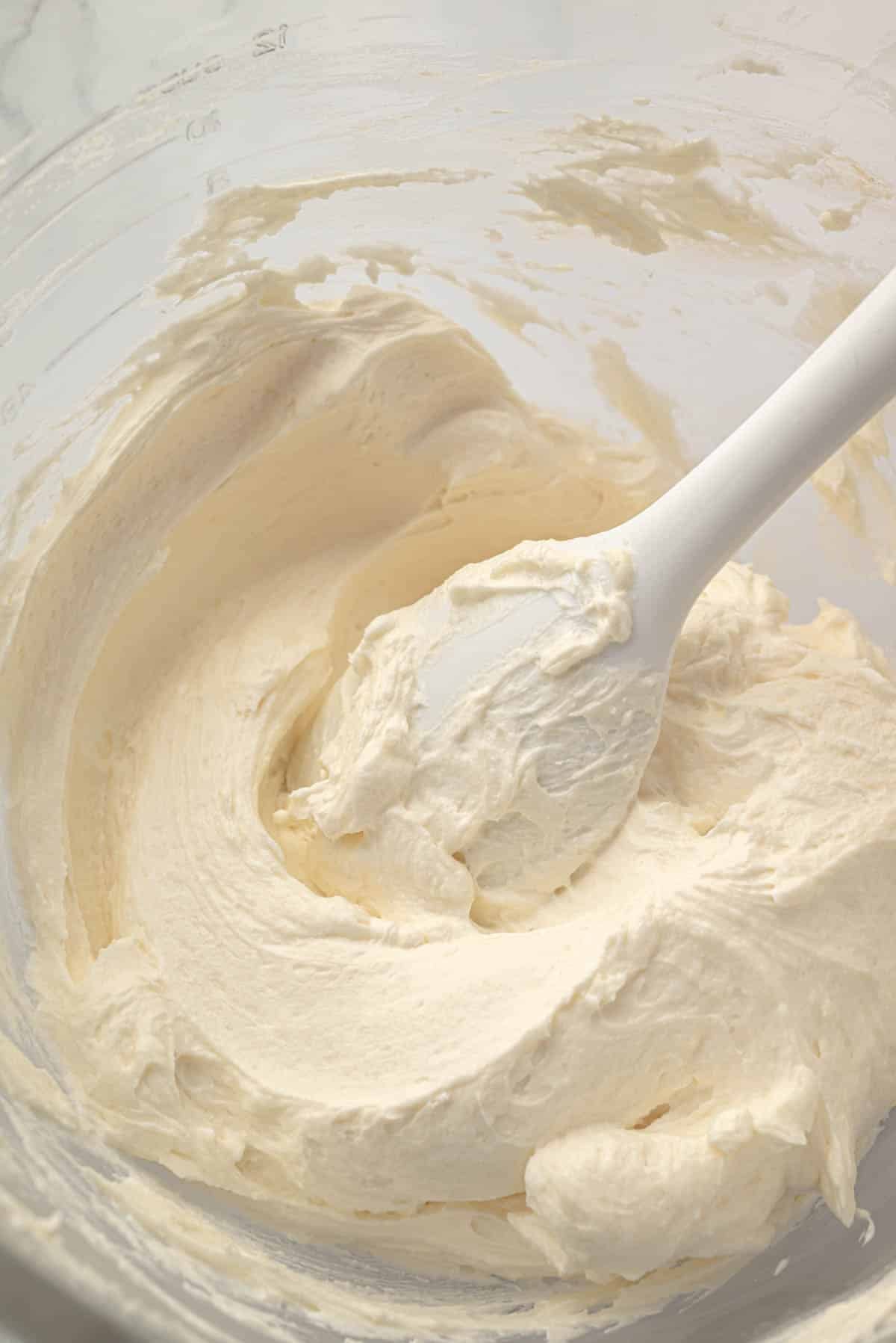 A glass mixing bowl with ermine frosting. A white spatula is resting in the side of the bowl.