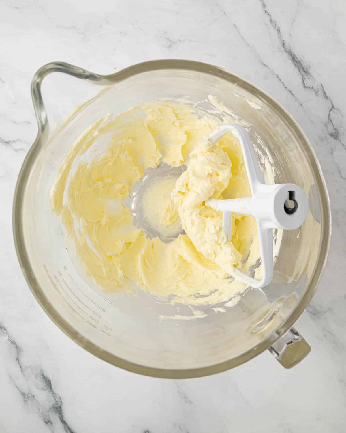 A glass mixing bowl with creamed butter and a paddle attachment.