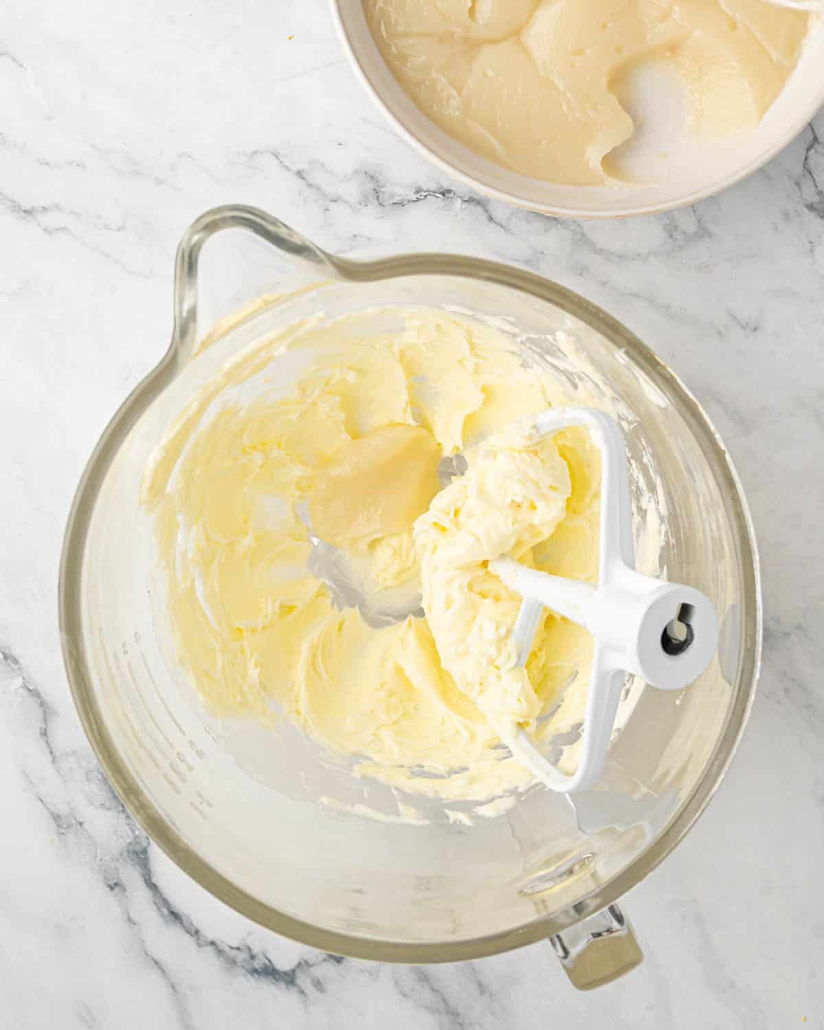A glass mixing bowl with creamed butter and some of the cooled roux added. Paddle attachment is to the side.