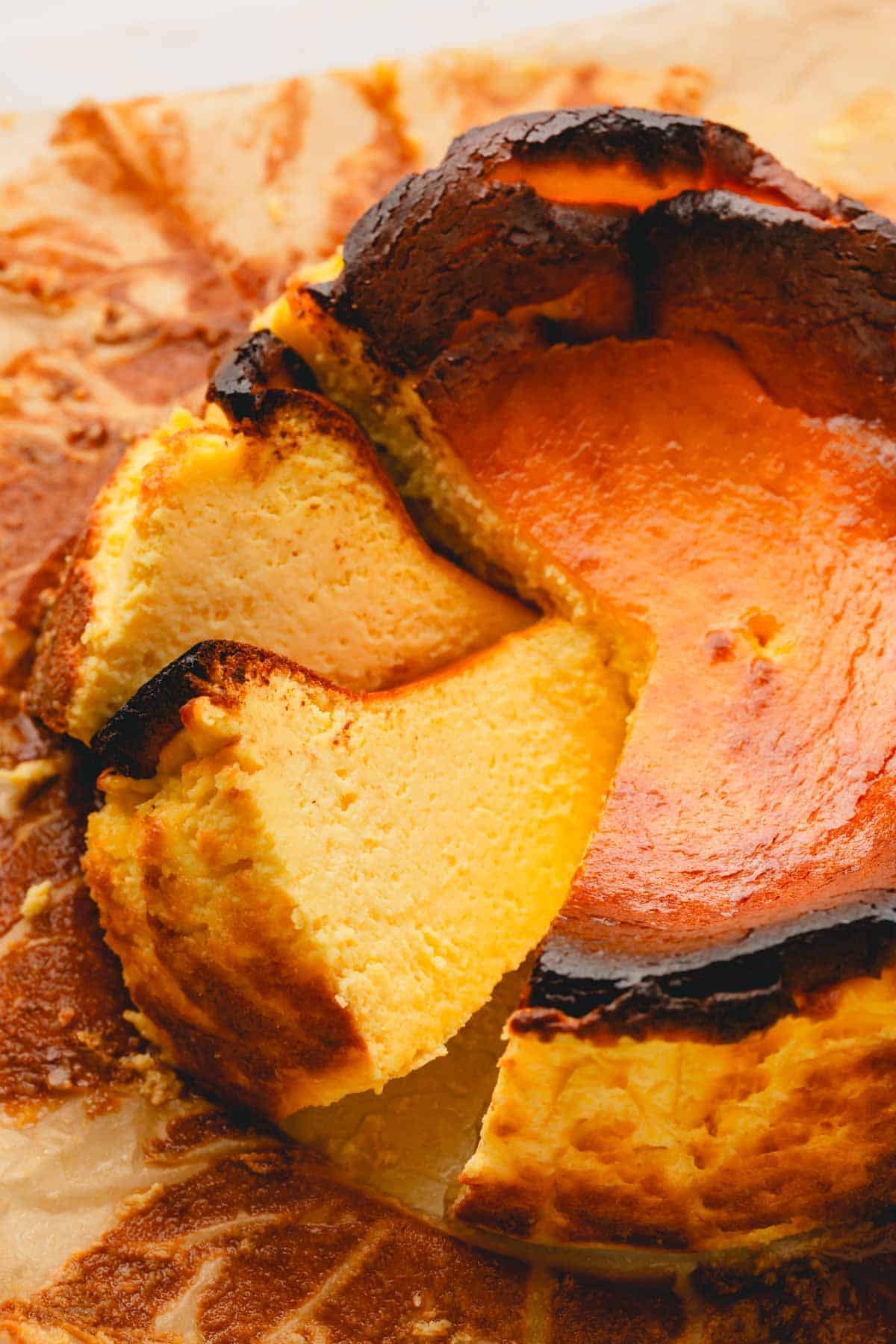 A whole basque cheesecake on a baking paper with 2 slices cut.