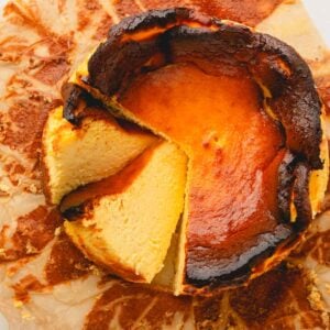 A whole basque cheesecake on a baking paper with 2 slices cut.